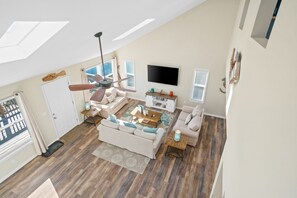 A spacious living room with a high ceiling, a ceiling fan, a flat-screen TV, and a large window. - 2 minute walk to the beach, stores and restaurants (Cape San Blas)