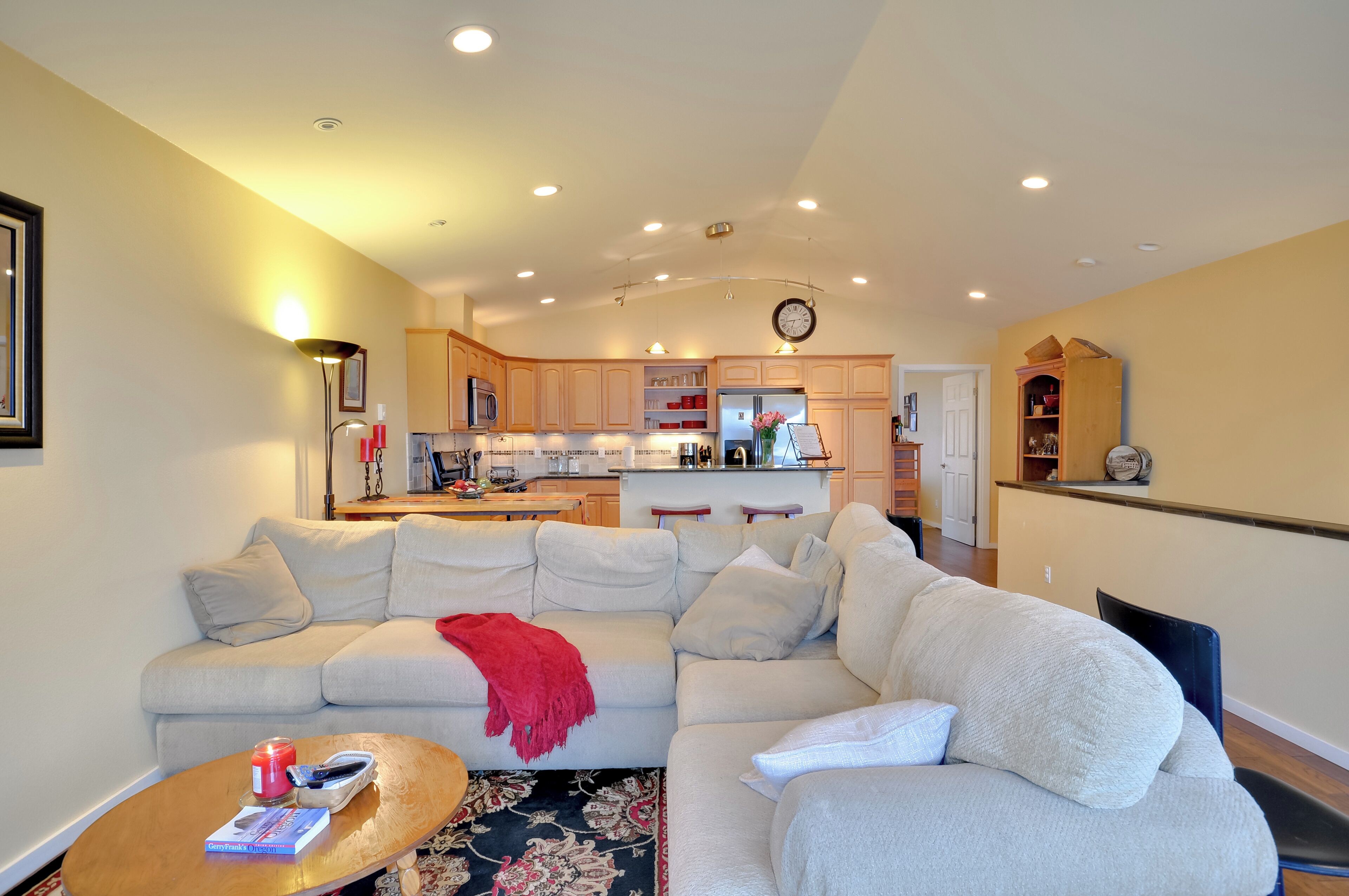A modern living room with a large sectional sofa, a coffee table, and a kitchen in the background.