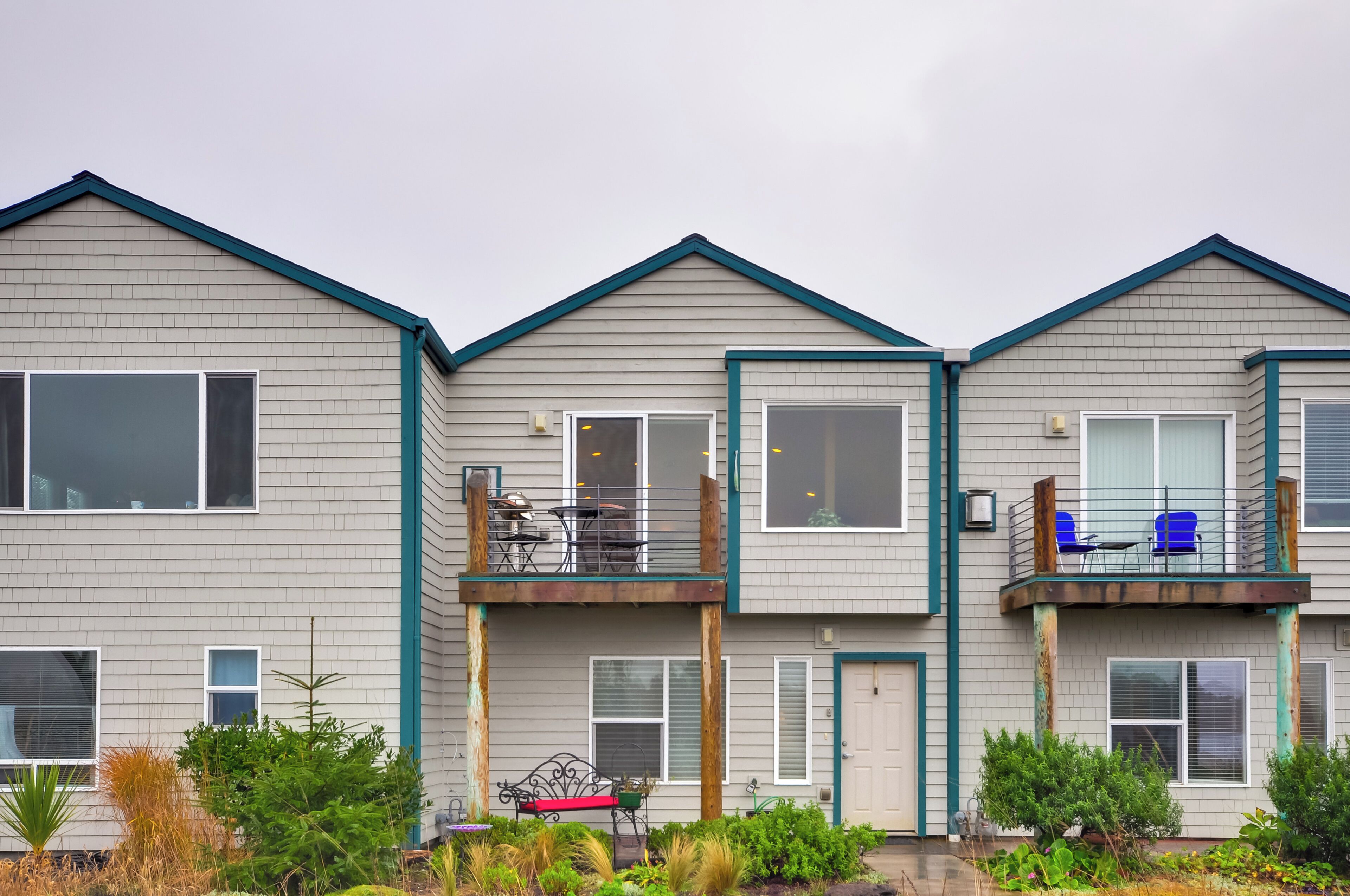 A row of townhouses with a balcony, a small garden area, and a metal bench.