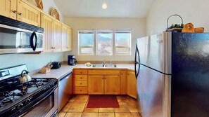 A kitchen with wooden cabinets, a stainless steel refrigerator, a gas stove, and a window with a view. - Desert Hideaway - C2, Enjoy The Views (Moab)
