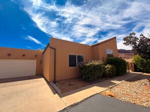 A residential building with a garage, a small window, and a well-maintained garden with shrubs and a gravel driveway. - Desert Hideaway - C2, Enjoy The Views (Moab)