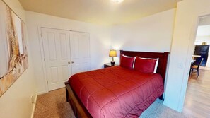 A bedroom with a bed, a nightstand, a lamp, a door, and a chair. - Desert Hideaway - C2, Enjoy The Views (Moab)