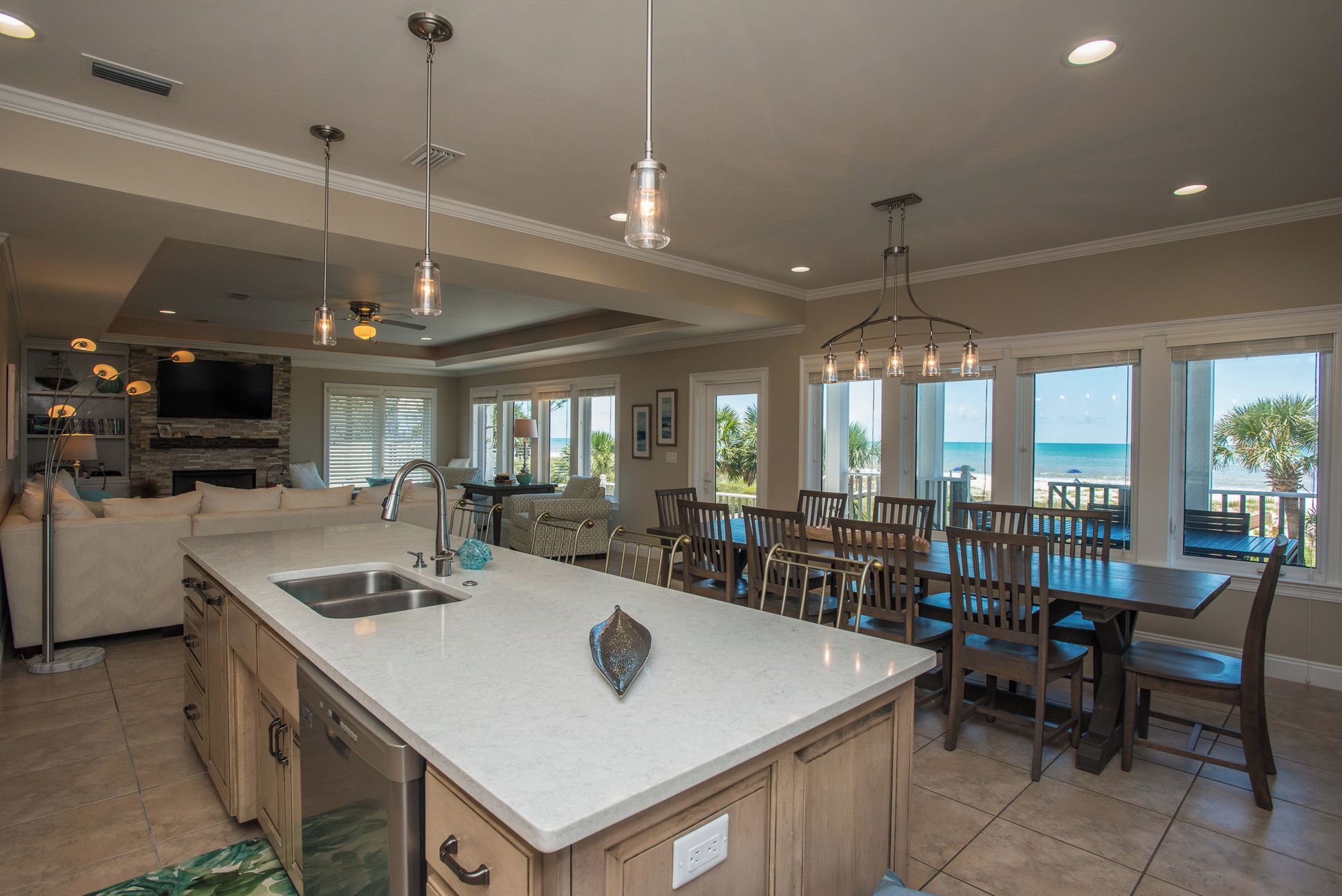 A spacious kitchen with a large island, a dining area with wooden chairs, and a view of the ocean.
