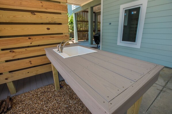 A wooden outdoor kitchen with a sink and faucet, a window, and a door leading to a covered porch. - Gulf Front, Pool & Elevator, 5bdrm (Indian Pass)