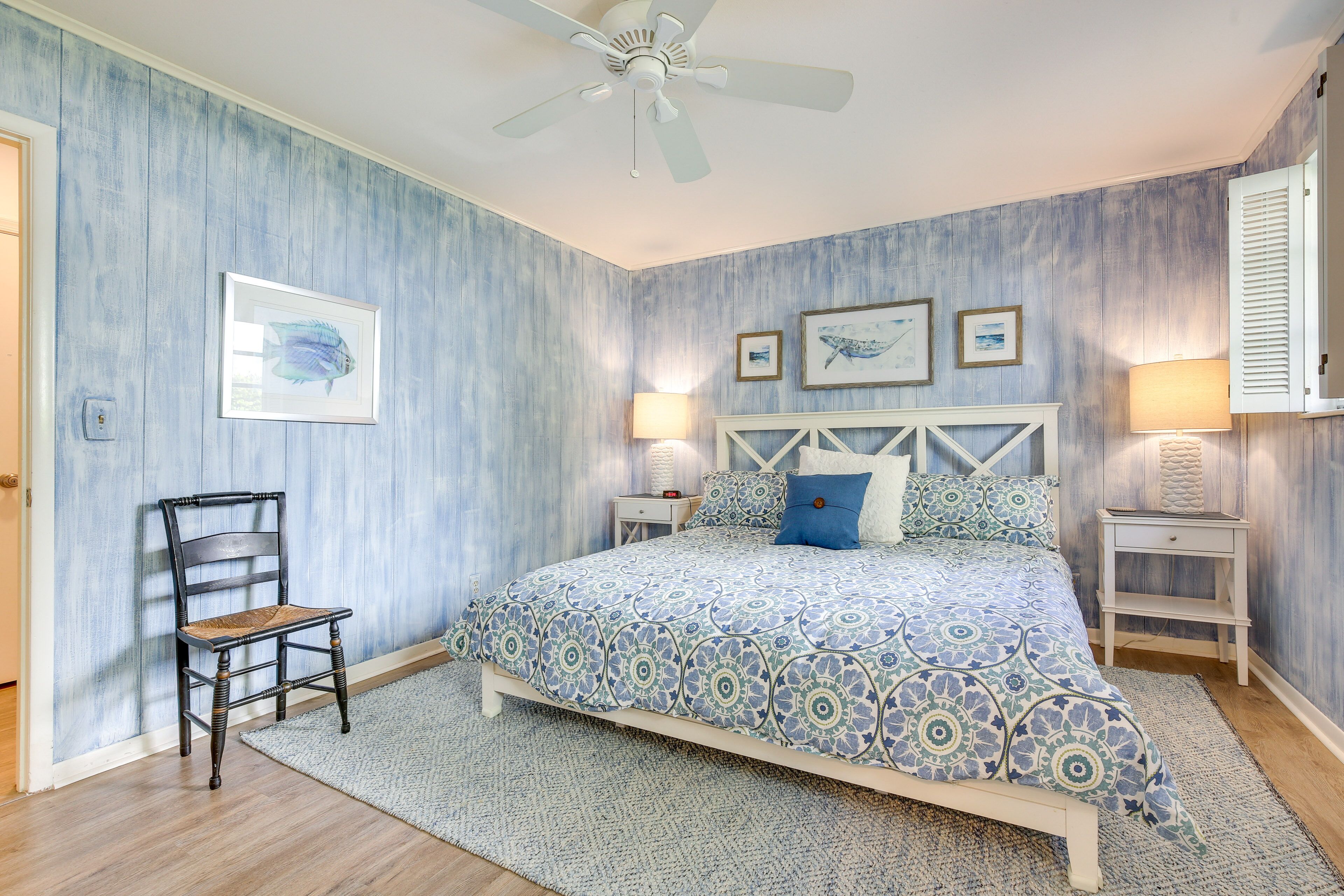 A bedroom with a bed, a chair, a nightstand, a lamp, and wall art.