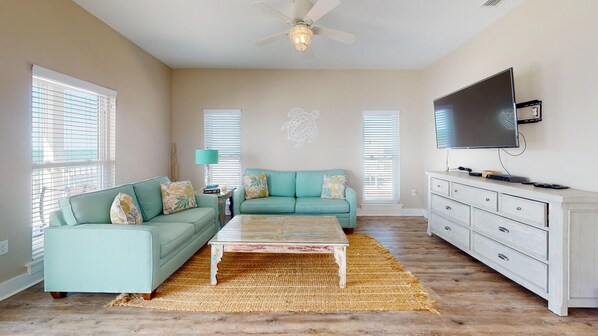 A spacious living room with a teal sofa, a coffee table, a white dresser, and a flat-screen TV. - Gulf Front! Elevator! Just steps to the ocean! (Cape San Blas)