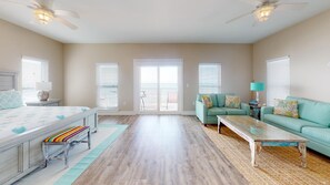 A spacious living room with a large sofa, a coffee table, and a bed with a colorful bench. - Gulf Front! Elevator! Just steps to the ocean! (Cape San Blas)