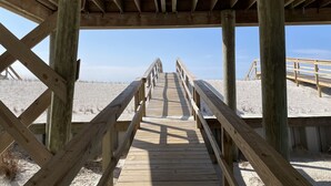Ein hölzerner Steg führt zu einem Strandabschnitt unter blauem Himmel.