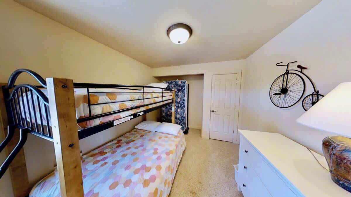 A bedroom with a bunk bed, a bedside table, a lamp, and a bicycle mounted on the wall.