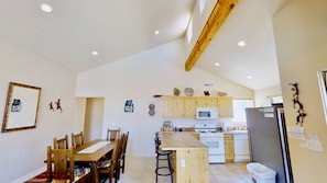 A kitchen with wooden cabinets, a microwave, a stove, and a refrigerator. There is a dining table with chairs and a small island with bar stools.