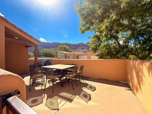 Eine Terrasse im Freien mit Tisch, Stühlen, einem Grill und Blick auf Berge.