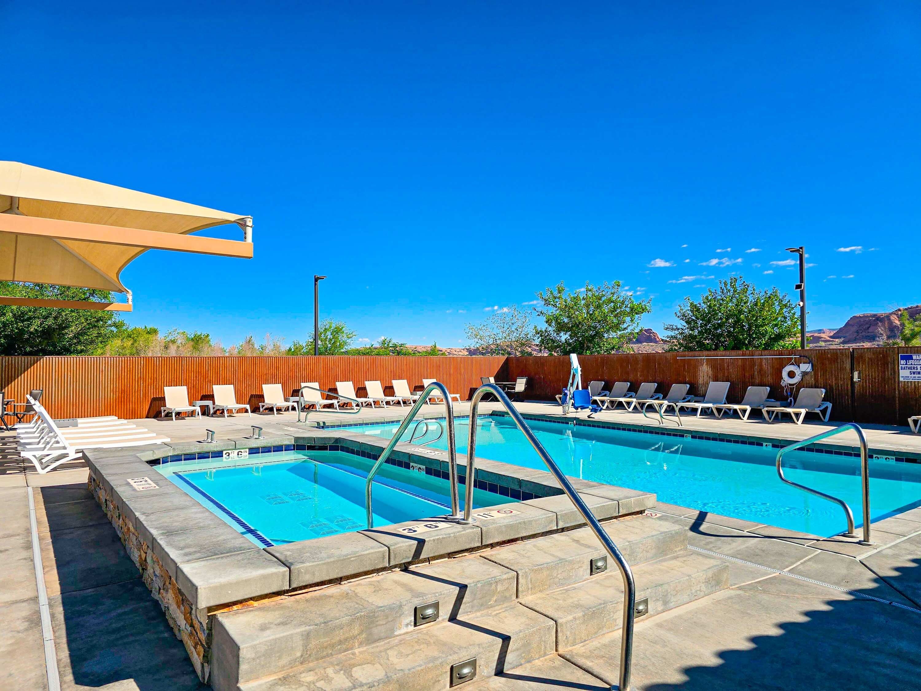 A pool area with two swimming pools, lounge chairs, and a wooden fence.