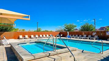 A pool area with two swimming pools, lounge chairs, and a wooden fence.
