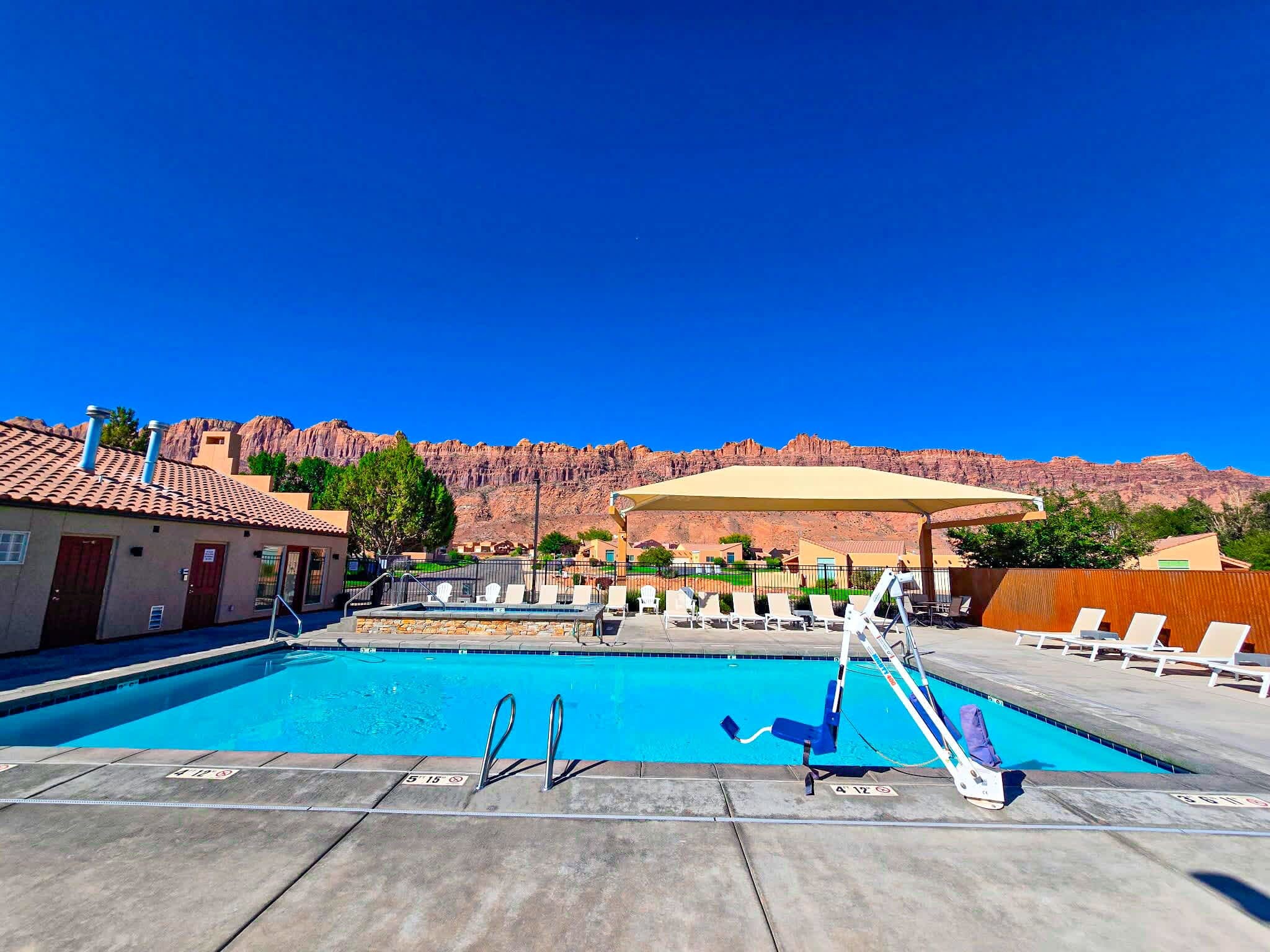 Ein Swimmingpool mit Sprungbrett, Liegestühlen und Blick auf rote Felsformationen.