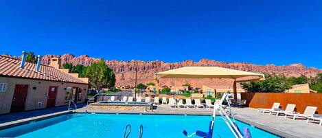 Una piscina con un trampolín, sillas de descanso y vistas a formaciones rocosas rojas.