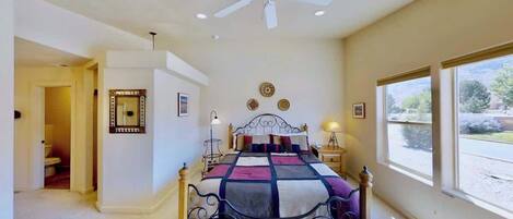 A bedroom with a bed, a ceiling fan, a window, and a door leading to another room.