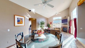 A dining area with a glass table, chairs, a ceiling fan, and a fireplace.
