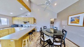 A modern kitchen with wooden cabinets, a central island with stools, a dining table with chairs, and a ceiling fan.