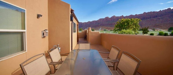 A balcony with a table and chairs, a window, and a view of mountains.