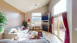 A living room with a sofa, a small table with a vase, a fireplace, and a large window with curtains.