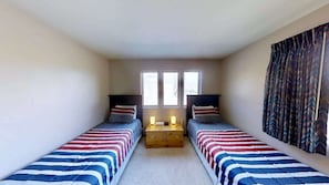 A room with two single beds, a nightstand, and a window with curtains.