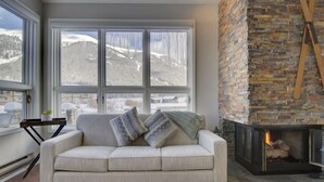 A cozy living room with a sofa, a fireplace, and large windows offering a view of snow-covered mountains. - Private Mountain Town home Pet Friendly - with Great Views! WD12 (Copper Mountain)