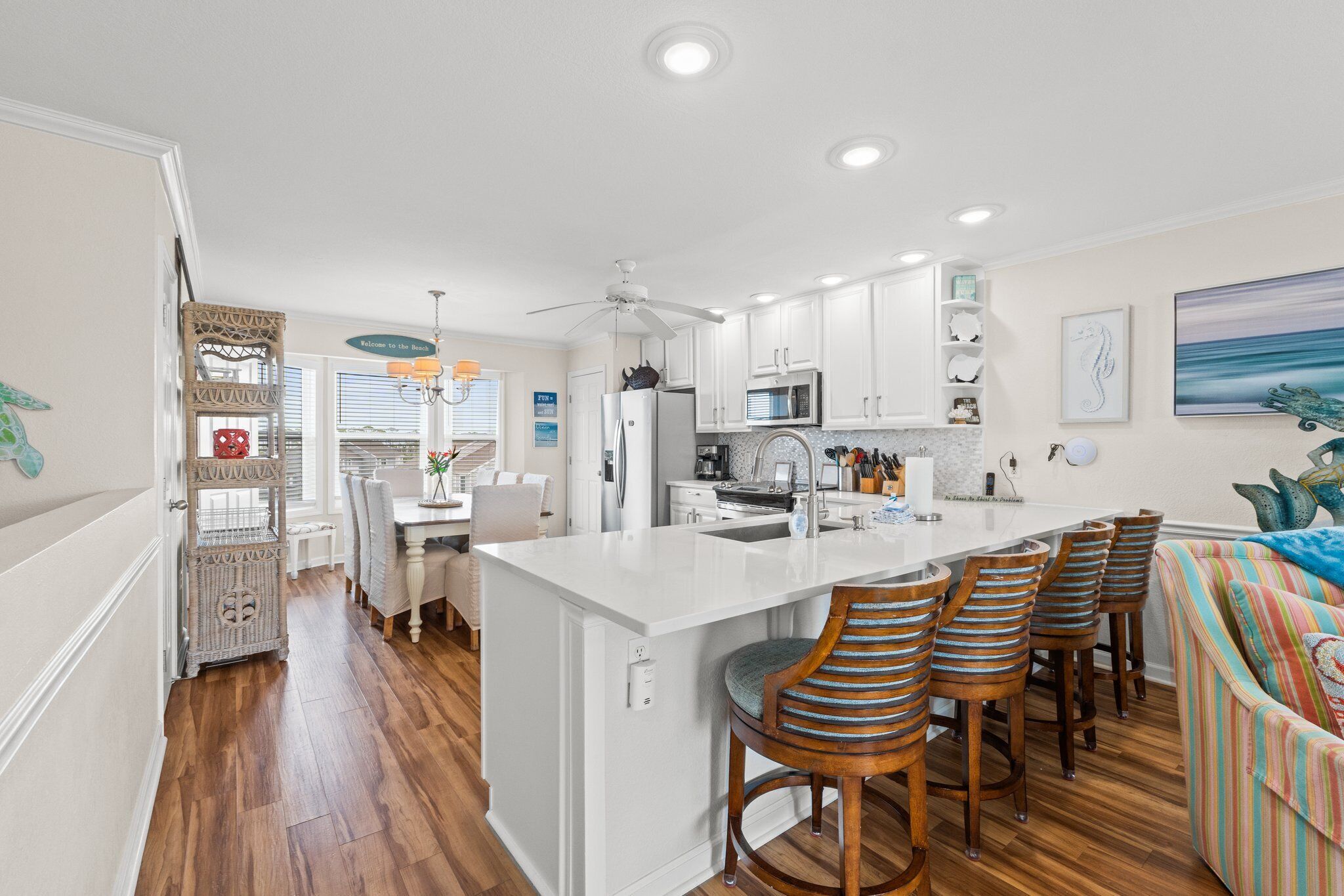 A modern kitchen with white cabinetry, a central island with bar stools, and a dining area with a white table and chairs.