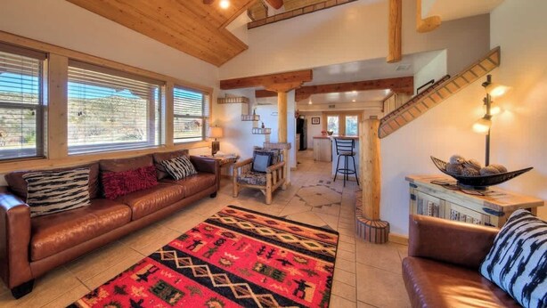 A spacious living area with a leather sofa, patterned rug, and a staircase with wooden railings. - Pack Creek - Orchard House, Beautiful Cabin (Moab)