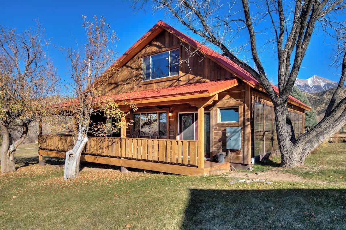Una baita di legno con tetto rosso, un portico e montagne sullo sfondo.