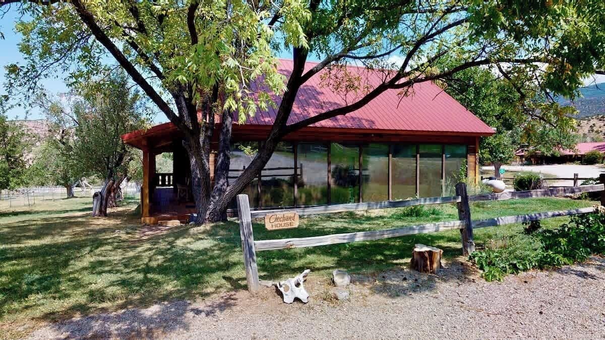 A rustic building with a red roof, a wooden fence, and a sign that reads 'Cheeseboard House.'