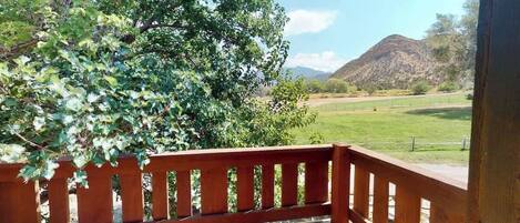 A wooden deck with a view of a grassy field and mountains in the distance.