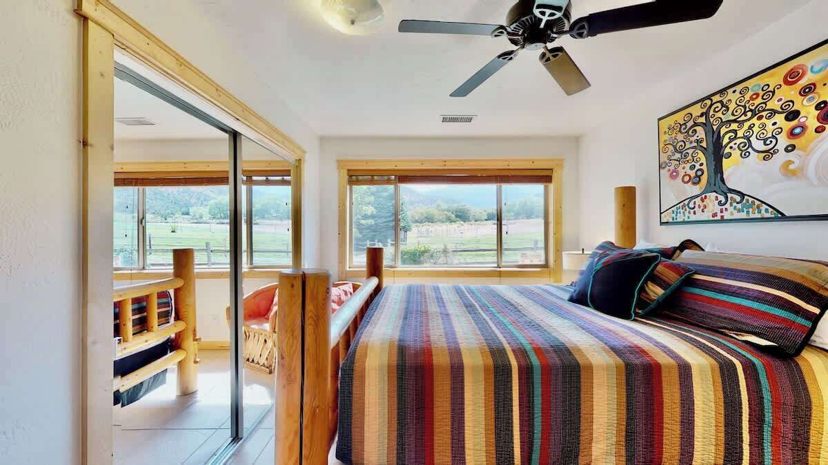 Un dormitorio con una cama grande, ventilador de techo y vistas al exterior a través de amplios ventanales.