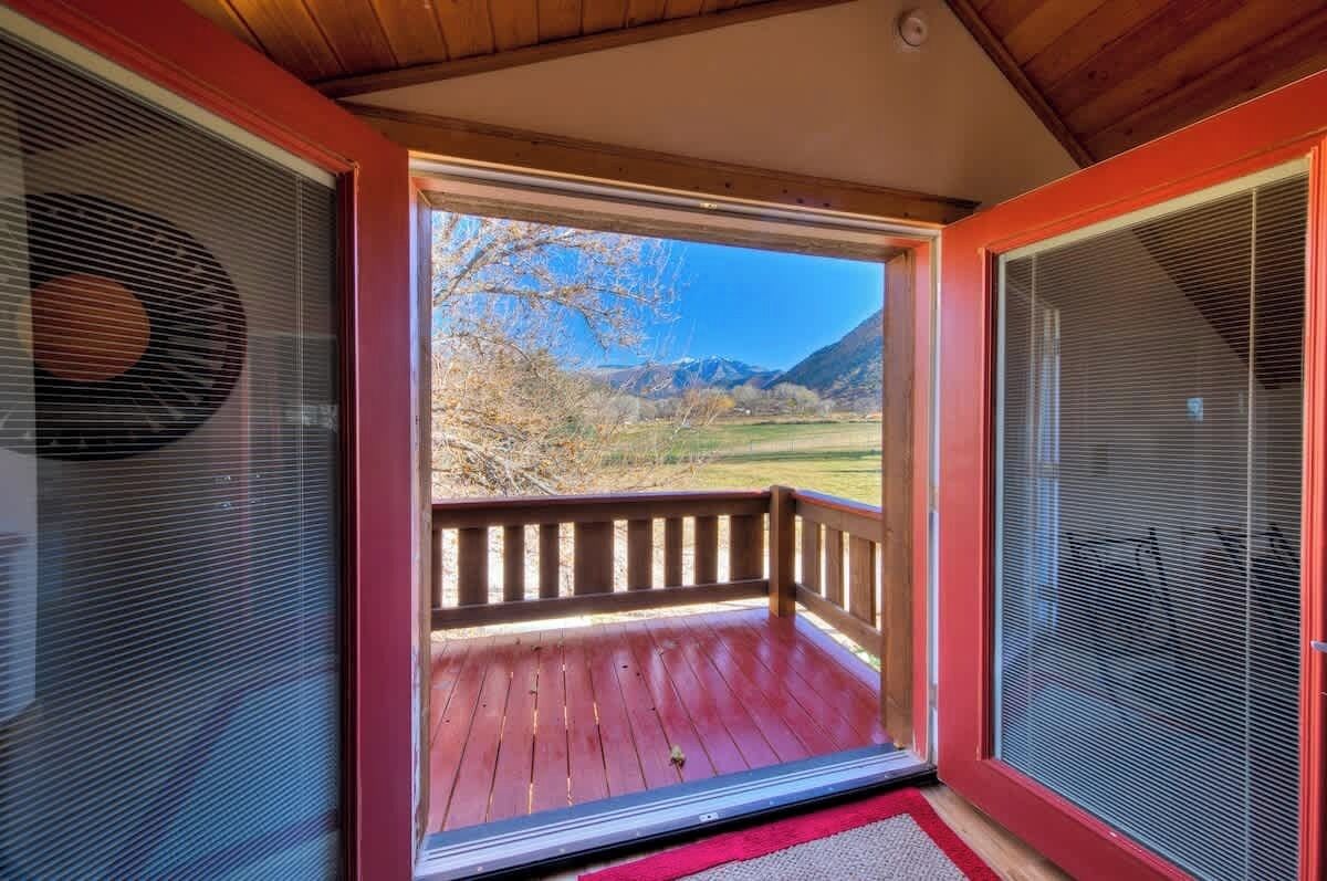 A wooden deck with a red railing, a clear view of a mountainous landscape, and a screened-in window on the right.
