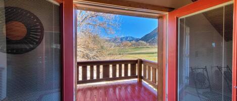 A wooden deck with a red railing, a clear view of a mountainous landscape, and a screened-in window on the right.