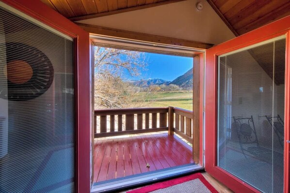 A wooden deck with a red railing, a clear view of a mountainous landscape, and a screened-in window on the right.