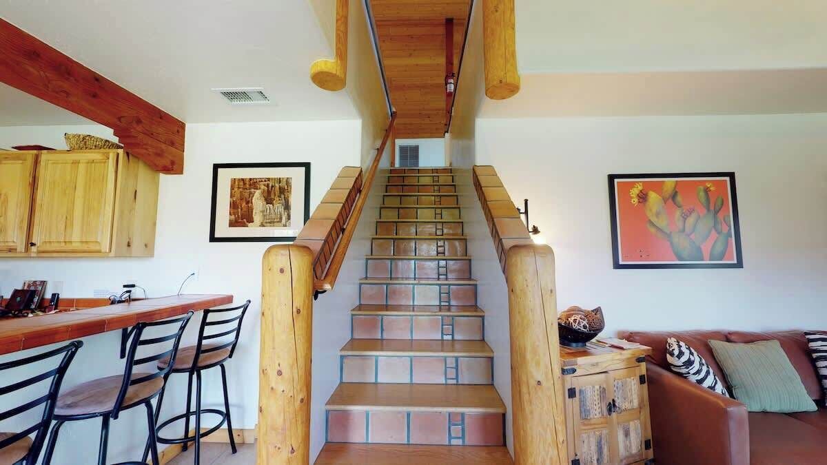 A staircase with wooden railings leading to a lower level, a wooden bar with chairs, and a couch with cushions.