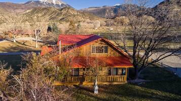 A wooden cabin with a red roof, surrounded by trees and mountains.