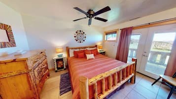 Quarto com cama, mesas de cabeceira, ventilador de teto, janela com cortinas e vista para o exterior.