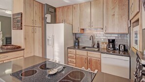 Een moderne keuken met houten kastjes, een witte koelkast, een inbouwoven en een koffiezetapparaat.