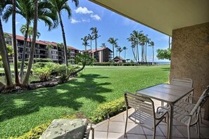 Une terrasse avec une table et des chaises, donnant sur une pelouse bien entretenue et un immeuble doté de nombreux balcons.