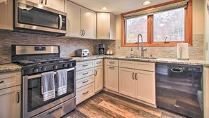 A modern kitchen with stainless steel appliances, a built-in oven, a dishwasher, and a window with a view of trees.