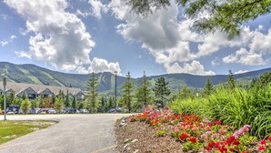 A parking lot with a building in the background, surrounded by greenery and mountains.