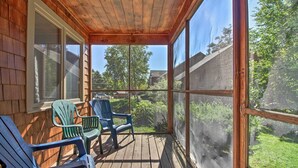 A wooden deck with two green Adirondack chairs and a view of a backyard.