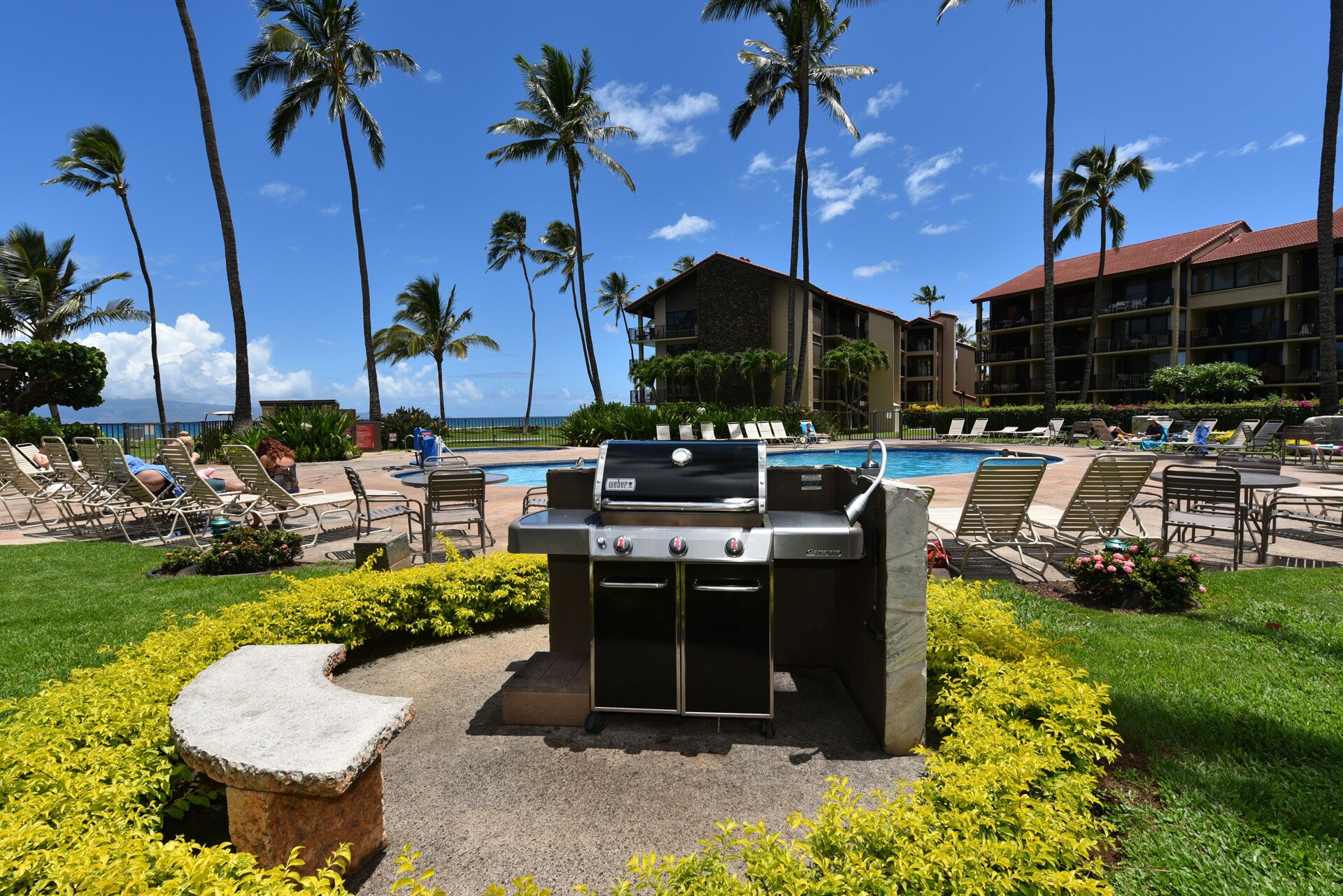 Ein Poolbereich mit einem Weber-Grill, Liegestühlen und Blick auf den Ozean.