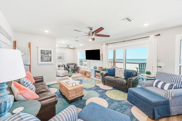 A spacious living room with a large window, a ceiling fan, and a flat-screen TV.