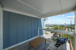 A balcony with a view of the beach, a wooden table, and a sofa with patterned cushions.