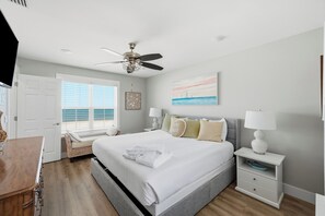 A bedroom with a bed, bedside tables, a ceiling fan, a window with blinds, and a painting on the wall.