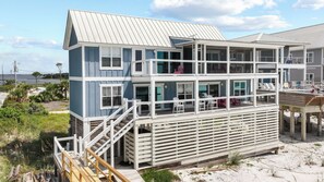 A multi-level beachfront house with a balcony, outdoor seating, and a view of the sea.