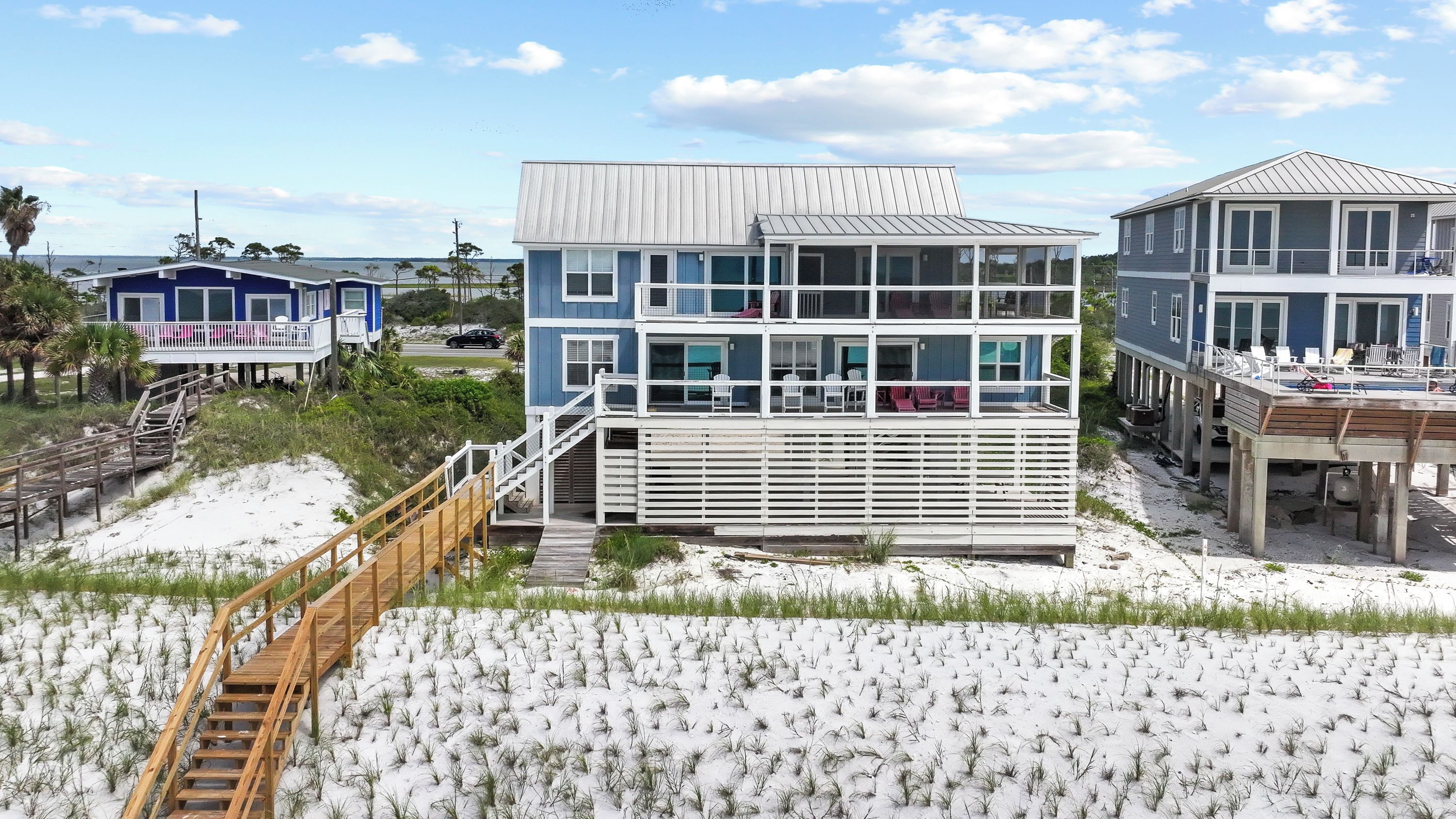 Une propriété située en bord de mer, comprenant un bâtiment à plusieurs niveaux, une terrasse en bois et un escalier menant à la plage.