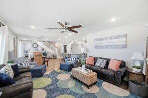Ein geräumiges Wohnzimmer mit Deckenventilator, einem großen Teppich mit kreisförmigen Mustern und einer Mischung aus Sofas und Sesseln.